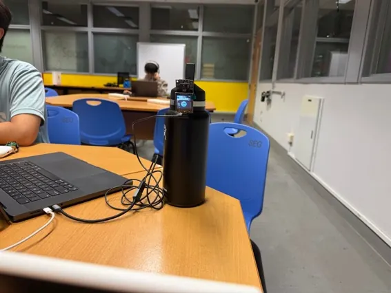 The ESP32-EYE reader on a bottle pointed at the MeterSim display, in a classroom
